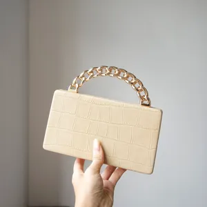 Close-up of elegant beige crocodile-textured leather mini handbag with chunky gold chain handle.