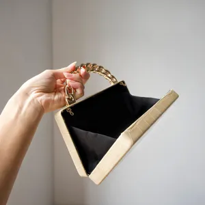 Detail view of a chic beige crocodile pattern clutch bag with gold chain handle and black lining.