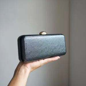 Detailed view of dark metallic texture hard case evening clutch bag with golden clasp.