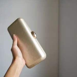 Close-up detail shot of a gold leather evening clutch bag with metallic clasp texture.