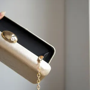 Golden metallic clutch bag with chain strap and clasp, elegant evening party accessory.