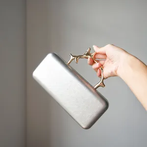 Detailed view of the elegant silver clutch bag featuring a luxurious gold branch metal handle.