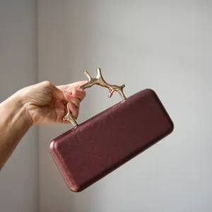 Detailed shot of a luxury burgundy leather evening clutch with unique gold metal branch handle.