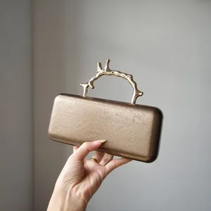 Close-up of luxury bronze leather evening clutch bag featuring a gold metallic branch handle.