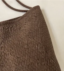 Nahaufnahme einer braunen geflochtenen Umhängetasche mit weicher Textur und Riemen.