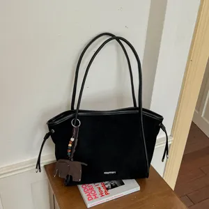 Vue détaillée d'un sac cabas en suédine noire avec de longues anses et un charm éléphant.