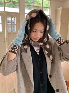 Detailed shot of knitted polka dot triangle scarf and gloves set in cozy indoor winter setting.