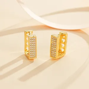 Detailed shot of fashionable geometric paved cubic zirconia huggie earrings in polished gold tone.