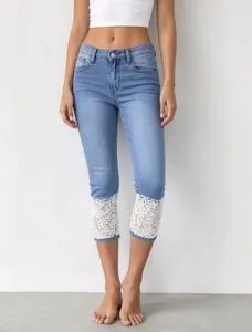 Close-up detail of women cropped denim jeans featuring elegant white lace hem trim design.