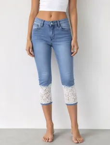 Detail view of light blue cropped denim jeans featuring elegant white lace cuffs and stretch fit.