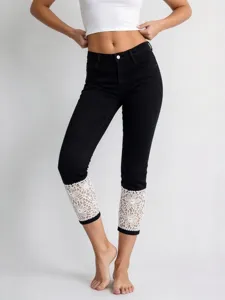 Detail view of women's black cropped denim jeans featuring elegant white lace cuffs.