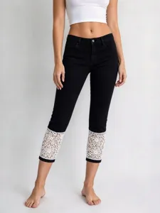 Detailed view of black cropped denim jeans featuring intricate white lace cuffs and stylish design.
