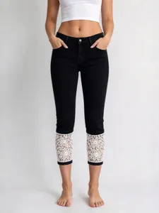 Women's cropped black denim jeans with elegant white floral lace trim cuffs, stylish design.
