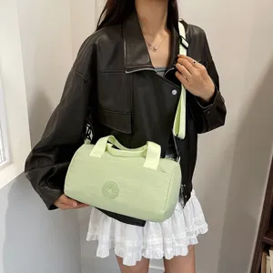 Sac bandoulière cylindrique vert clair avec double poignée et sangle pour les trajets quotidiens.