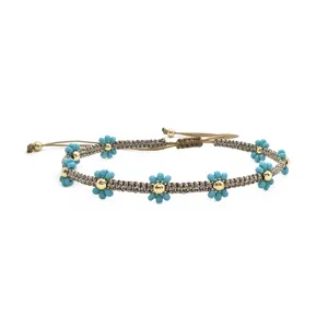 Primo piano sui dettagli del braccialetto boho in perline con margherite blu e sfere dorate.