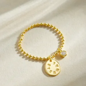 Gros plan sur la bague perlé dorée avec zircon serti clos et pendentif gravé de lettres.