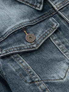 Gros plan sur la poche d'une veste en jean bleue vintage avec surpiqures et bouton metal.