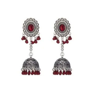 Primer plano de pendientes jhumka plateados con patrones calados y borlas de cuentas rojas.