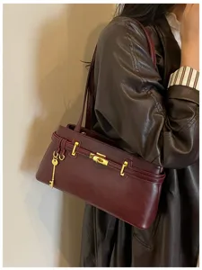 Détail de sac porté épaule en cuir bordeaux, serrure dorée élégante, style minimaliste.