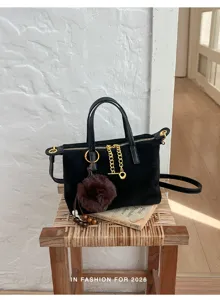 Close-up detail of black suede crossbody bag with gold chain and fluffy pom-pom charm.