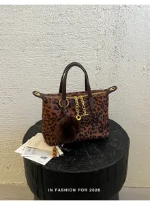 Detailed shot of a stylish leopard print handbag featuring a fluffy pom-pom charm and chain.