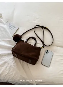 Detailed view of dark brown suede shoulder bag with fluffy pom-pom charm on clean bed.