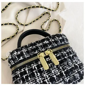 Detailopname van de zwart-witte tweed mini handtas met gouden ketting en handvat.