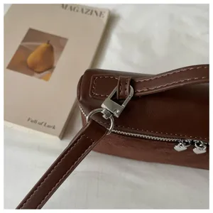 Primer plano de bolso bandolera marrón con cuero PU, ante y cremalleras en forma de corazón.
