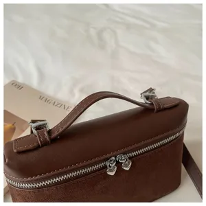 Vista detallada de un elegante bolso tipo caja marrón con atractivas cremalleras de metal.