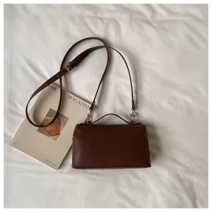 Vista detallada del elegante bolso de hombro marrón con asa y correa sobre tela texturizada.