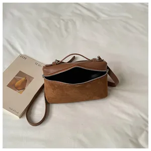 Bolso cruzado tipo caja de cuero y ante marrón, vista detallada de la textura y apertura.