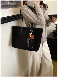 Zwarte suède shopper tas detail met houten kralen hanger en minimalistisch design.