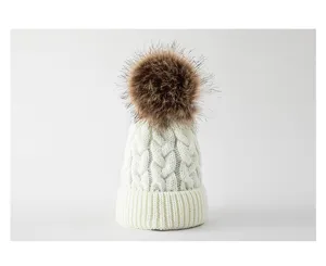 Detailaufnahme der Zopfstrickstruktur und des flauschigen braunen Bommels der Babymütze.