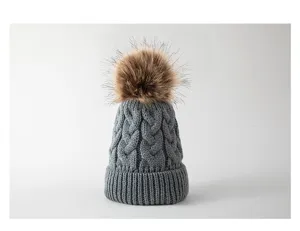 Nahaufnahme der grauen Babymütze mit Zopfmuster und flauschigem Kunstfell-Bommel.