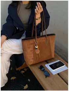 Gedetailleerd overzicht van bruine suède tote tas met houten hanger in streetwear stijlen.