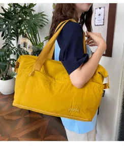 Detail view of a large yellow canvas travel duffel bag with shoulder straps and front pocket.