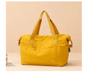 Detail view of the yellow travel tote bag, showing front pocket and durable handles.