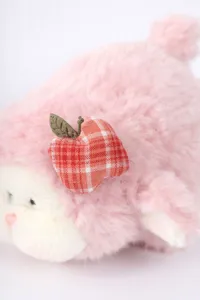 Nahaufnahme eines süßen rosa Plüschlamm-Spielzeugs mit weicher Textur und rotem Apfel.