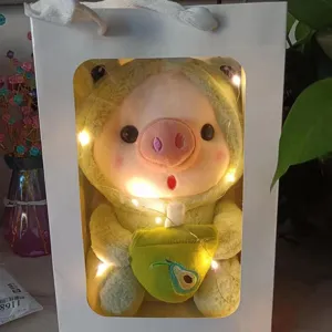 Cute plush pig doll toy wearing frog costume holding avocado bag in gift box with lights