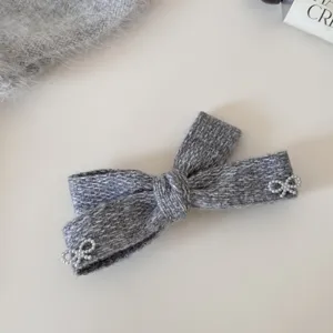 Primo piano della molletta per capelli a fiocco in maglia grigia con perle, elegante accessorio.