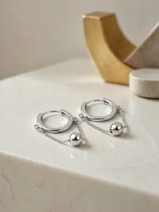 Nahaufnahme Detail von Silber Creolen mit hängender Kugel und Kette für modernen Schmuckstil.