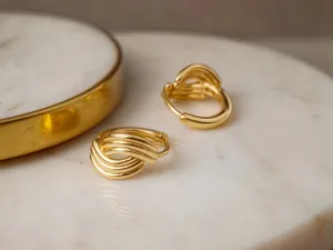 Detailaufnahme mehrschichtiger, stromlinienförmiger Gold-Ohrringe auf einer Marmorplatte.