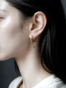 Nahaufnahme Detailansicht eines goldenen Creolen Ohrrings mit Kette und Perle am Ohr.