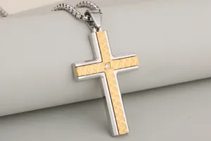 Stainless steel cross pendant close-up, featuring a two-tone silver and gold textured design.