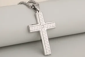 Stainless steel cross pendant detail shot showing textured geometric pattern and center stone.