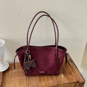 Gros plan du sac cabas en suédine bordeaux avec son charm éléphant et logo métallique.