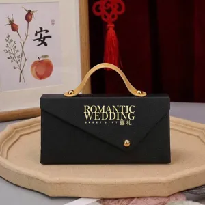Black wedding favor box detail shot, elegant gift bag with gold handle for party celebration.