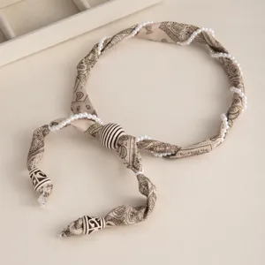 Gros plan sur le collier ras du cou en tissu paisley beige avec perles et bois.