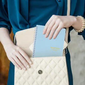 Detailansicht des hellblauen A5 Spiral-Wochenplaners, der in eine Handtasche gelegt wird.