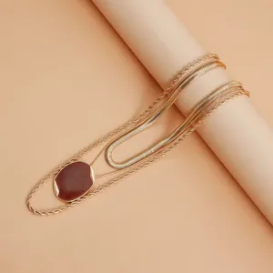 Splendida collana dorata multistrato con ciondolo ovale rosso vino e eleganti catene a serpente.